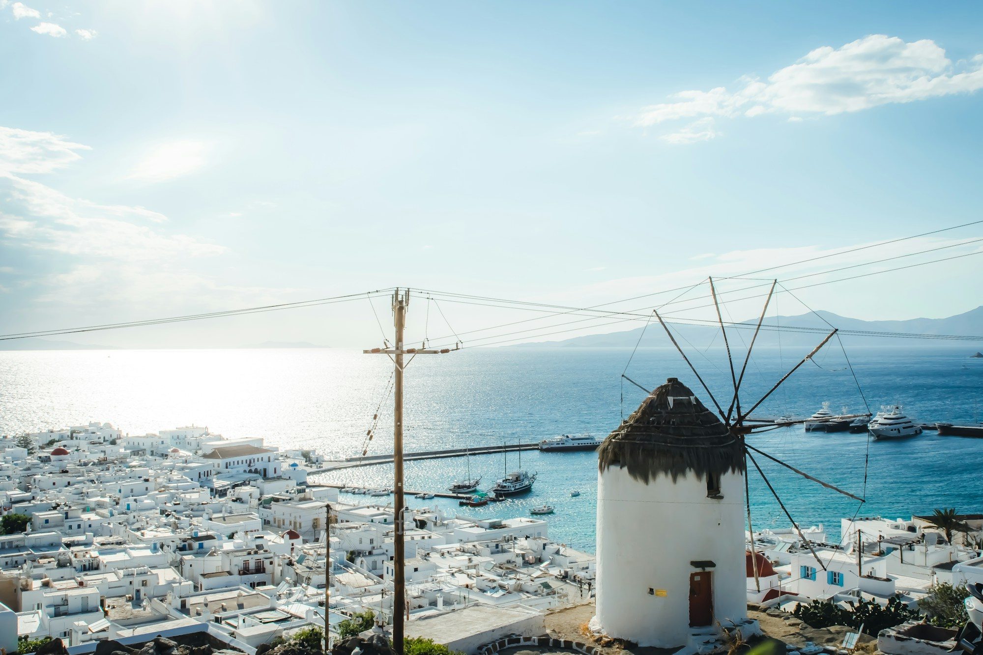A windmill above the white town and harbour of Mykonos at golden hour