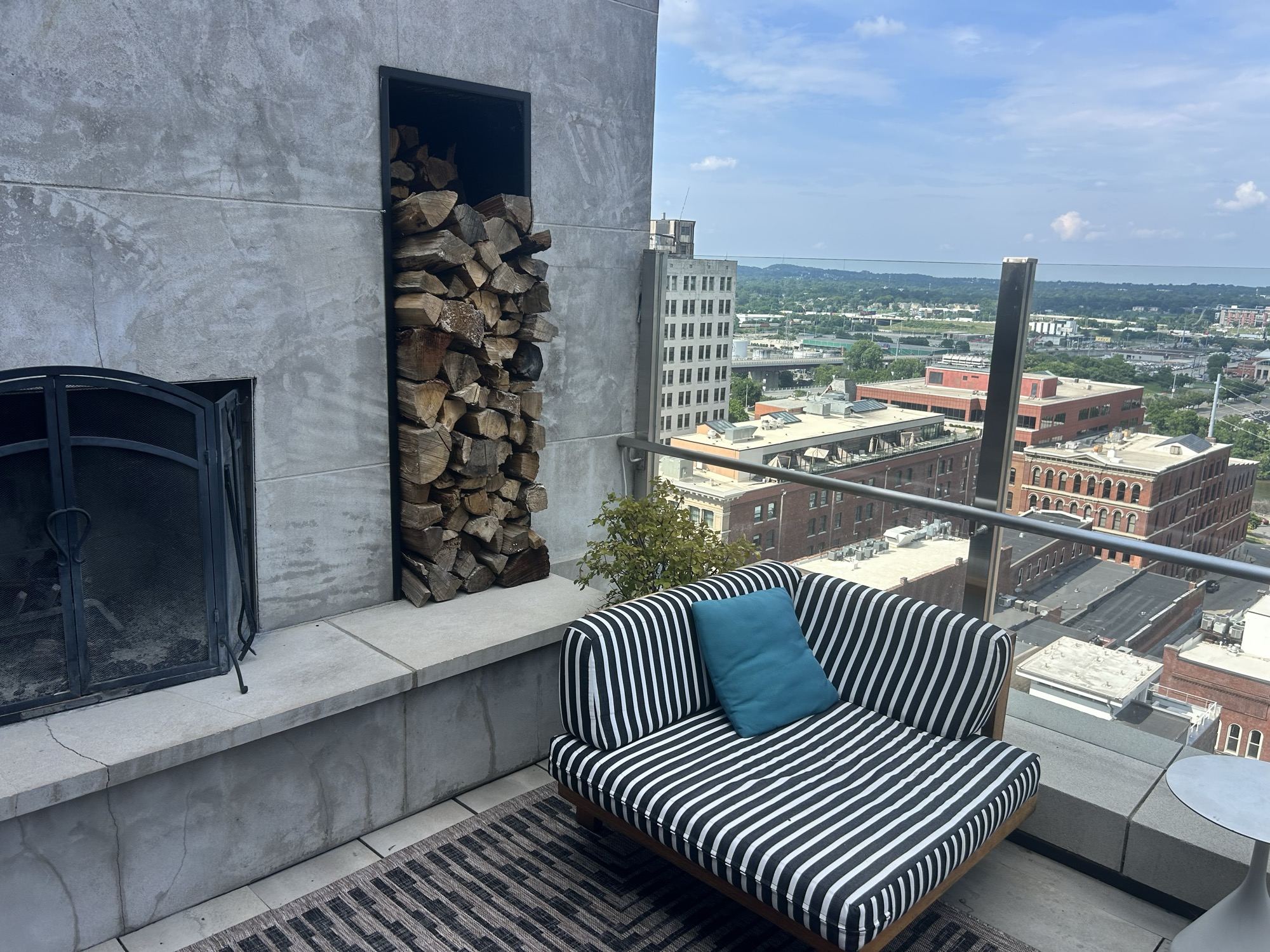 A striped rooftop settee beside a stone fireplace stacked with firewood, the downtown Nashville skyline beyond.