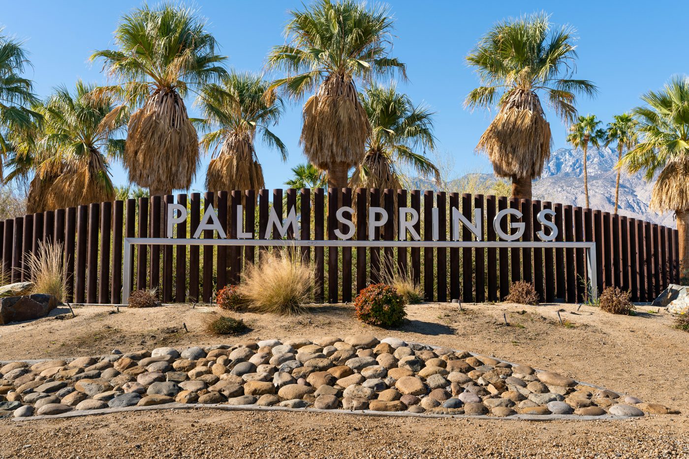 The Palm Springs entrance sign framed by tall palms with the San Jacinto mountains behind
