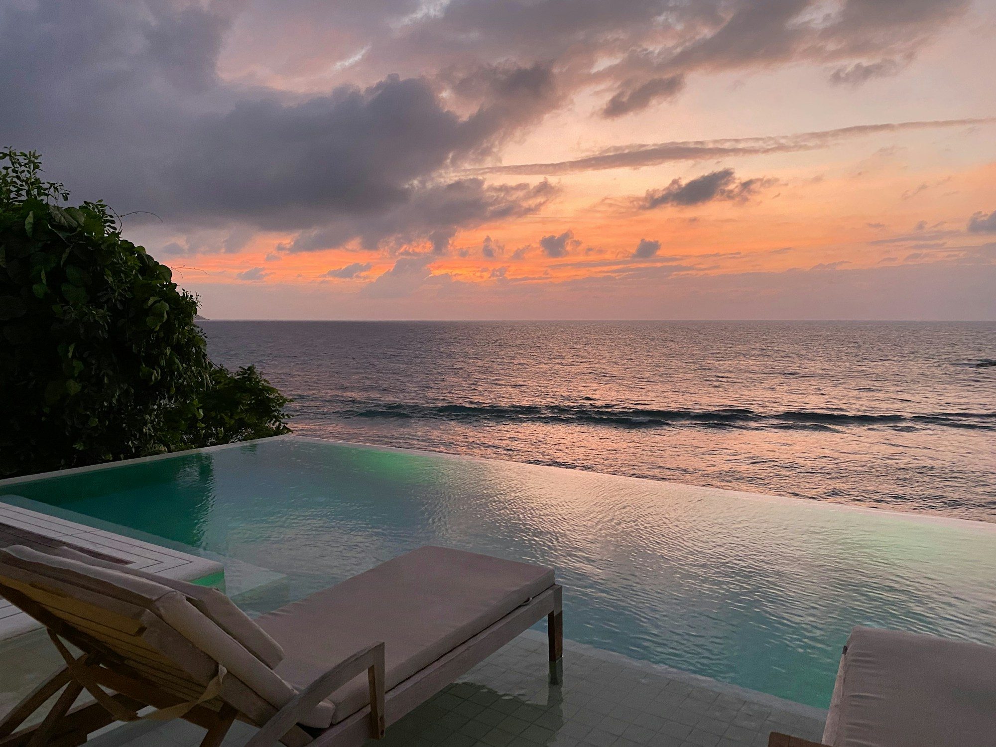 An infinity pool and loungers overlooking the ocean at sunset